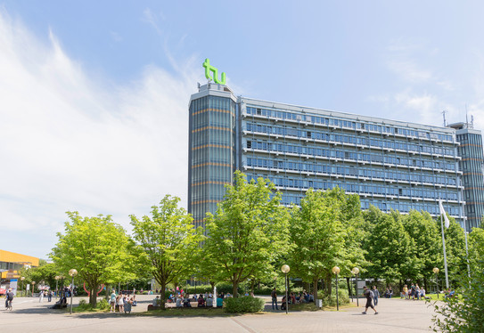 Campus Nord der TU Dortmund mit Blick auf den Mathetower an einem sonnigen Tag, im Vordergrund belaubte Bäume, 