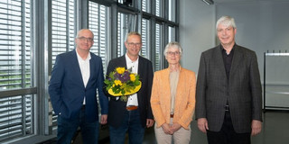 Four people standing next to each other. One man is holding a bouquet of flowers.